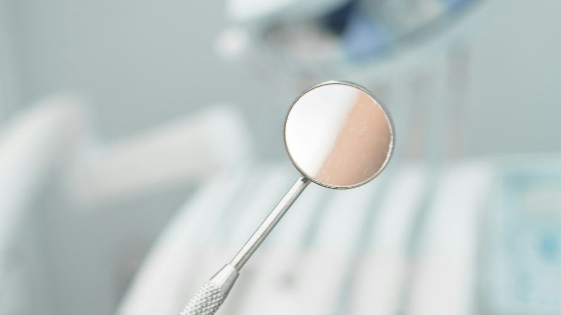 Espejo dental en primer plano con la unidad odontológica desenfocada al fondo
